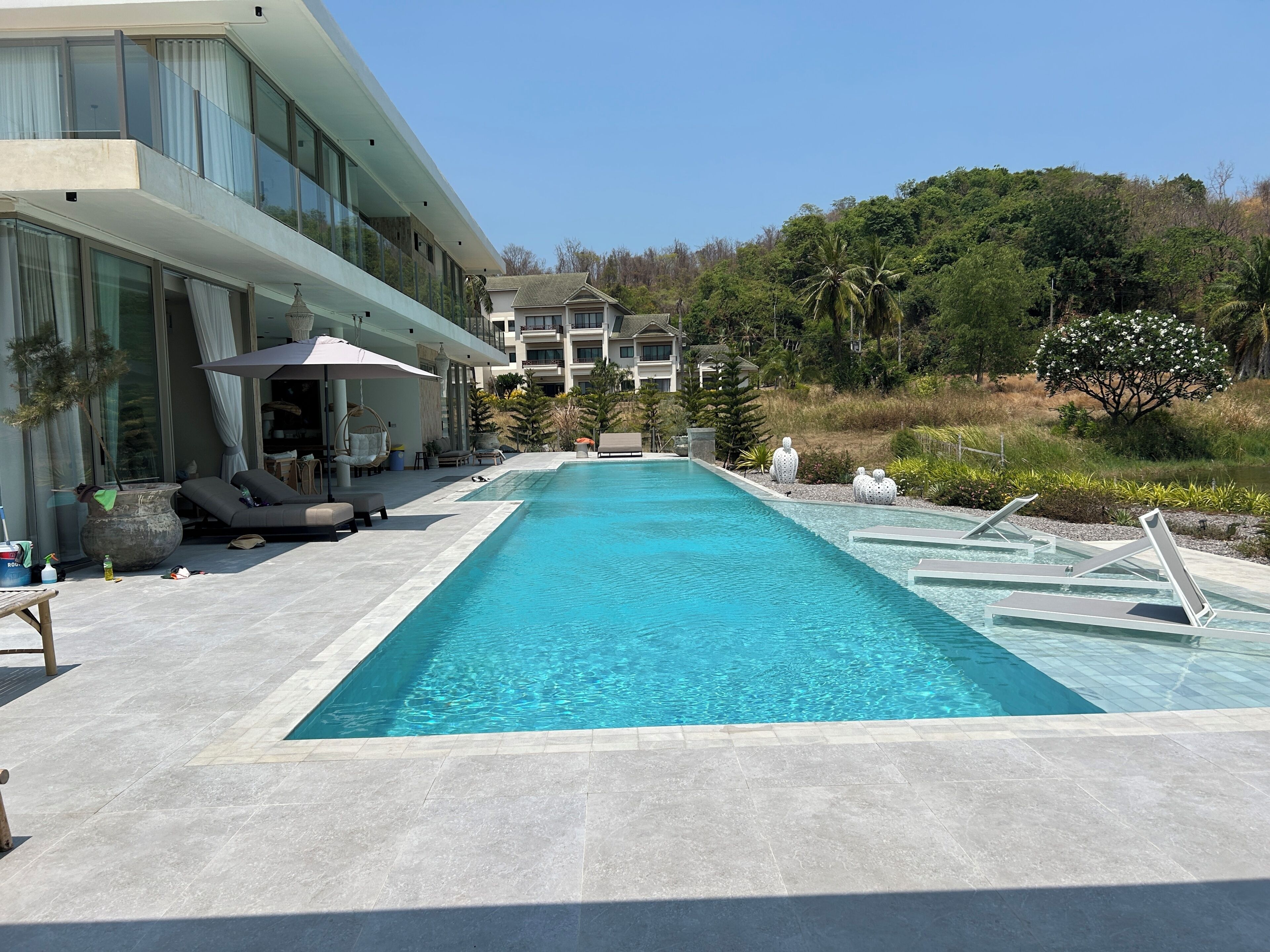 Ein modernes Hotel mit Schwimmbad, Sitzgelegenheiten im Freien und Blick auf die umliegende Grünfläche.