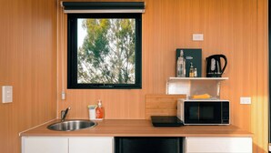 A compact kitchen with a sink, a microwave, a kettle, and a window with a view of trees.
