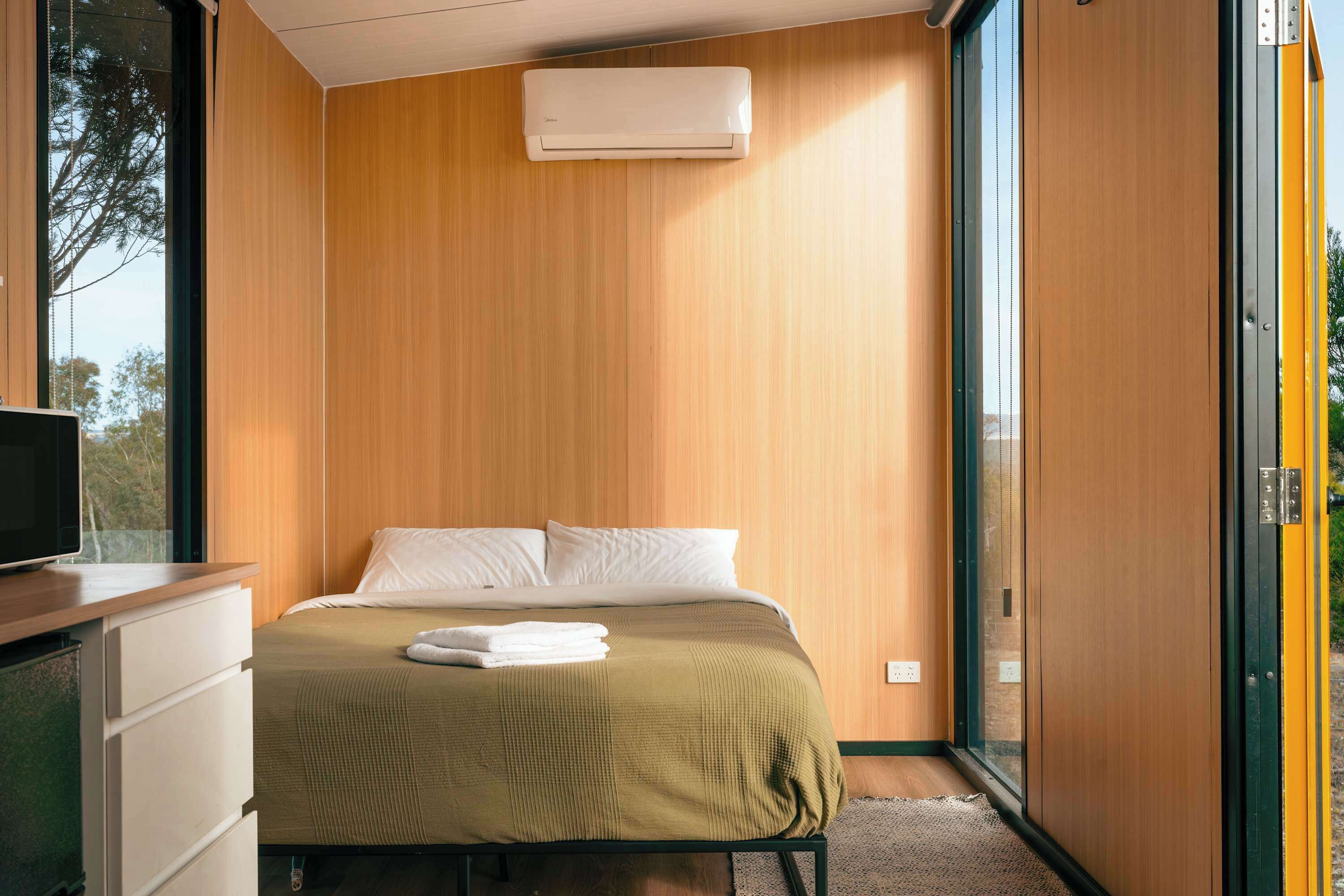 A bedroom with a bed, a TV on a dresser, and a window with a view of trees.