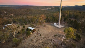 A large wind turbine in a rural setting with sparse vegetation and a few small buildings.