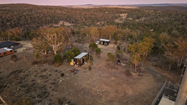 A remote cabin with a solar panel array, surrounded by forested hills.