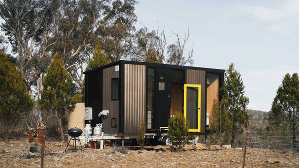 A modern, compact cabin with a large sliding door, a barbecue setup, and a water tank.