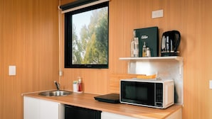 A compact kitchenette with a built-in microwave, a coffee maker, and a small shelf with a bottle and a glass.