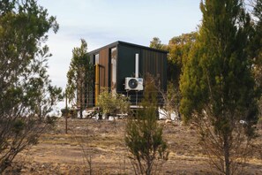 A modern building with a large air conditioning unit, surrounded by sparse vegetation and a fence.
