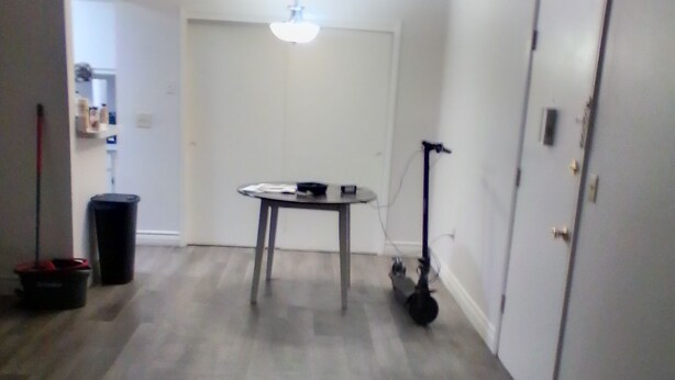Ein Zimmer mit Deckenventilator, Tisch mit Stuhl, Mülleimer und Tür.