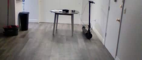 Une pièce avec un ventilateur de plafond, une table avec une chaise, une poubelle et une porte.