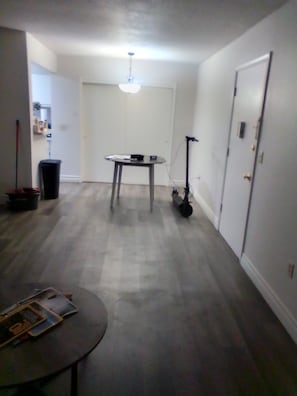 A room with a ceiling fan, a table with a chair, a trash can, and a door.