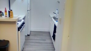 Eine schmale Küche mit weißen Schränken, einem Herd und einem Kühlschrank.
