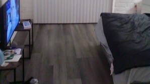Ein Hotelzimmer mit Bett, Fernseher auf einem Schrank, einer weißen Ziegelwand und einem Fenster mit Jalousien.