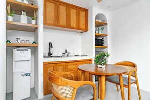 Cocina compacta con armarios de madera, un refrigerador, un lavamanos y un comedor con dos sillas y una mesa.