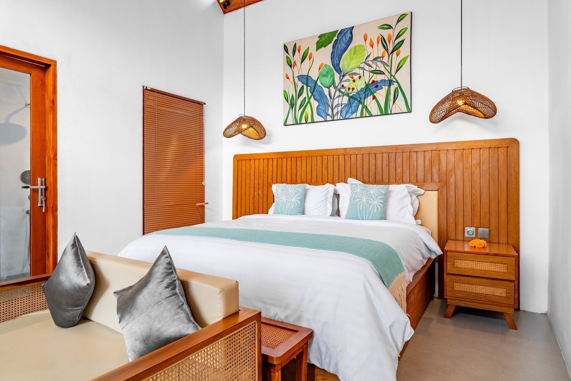 A bedroom with a wooden headboard, a bed with white bedding, a nightstand, a wall-mounted artwork, and a door with a wooden frame.