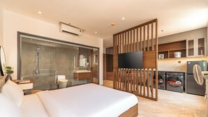 Quarto de hotel moderno com uma cama grande, chuveiro, televisão e uma cozinha compacta.