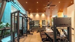 Uma academia com equipamentos de musculação, esteiras e um ventilador de teto.