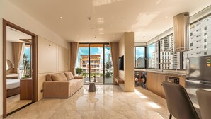 Quarto de hotel moderno com área de estar, sofá, mesa de centro, cozinha equipada com lava-louças e janelas amplas com vista para a cidade.