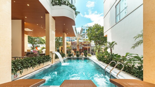 Piscina interna com espreguiçadeiras, cascata e vista para lojas próximas.