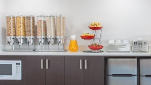 A kitchen with a microwave, cabinets, a toaster, and a fruit display. - TC Motel (Medicine Hat)