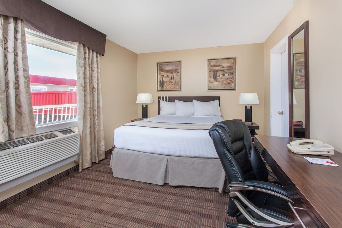 A hotel room with a bed, two bedside lamps, a desk with a telephone, and a chair.