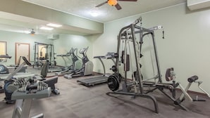A gym with exercise equipment, a ceiling fan, and a large mirror. - TC Motel (Medicine Hat)