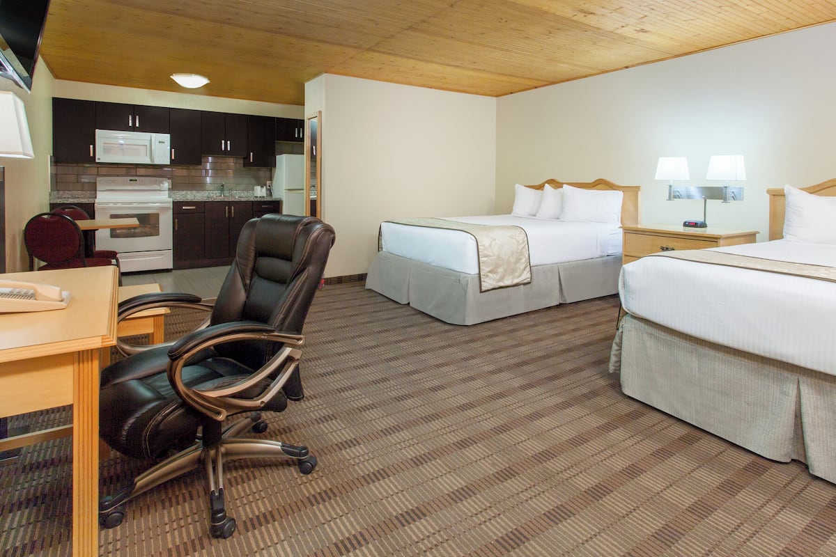 A hotel room with a bed, a desk, a chair, a microwave, and a small kitchenette.
