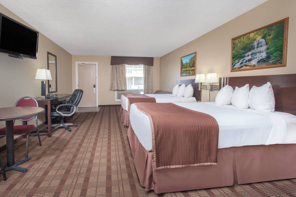A hotel room with a bed, a desk, a chair, a TV, and a painting on the wall.
