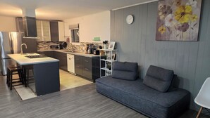 A modern kitchen with a central island, a dining area with a grey sofa, and a wall-mounted clock. - brossard home inn 1 (Brossard)