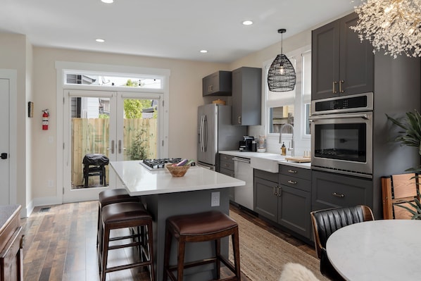 A modern kitchen with a central island, dark cabinets, stainless steel appliances, and a dining area with a round table and bar stools. - The Stella: The Star of the Short North! (Columbus)