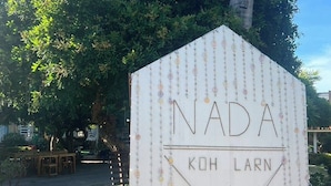 A white sign with 'NADA KOH LARN' written on it, surrounded by greenery. - Nada Koh Larn Resort (Koh Lan)