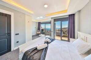 A hotel room with a bed, a small seating area, a balcony with a view, and a door.