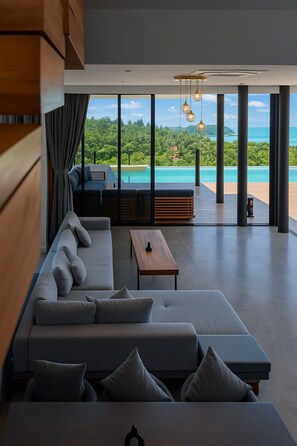 Una sala de estar moderna con un sofá grande, una mesa de centro de madera y vistas a un paisaje tropical.