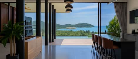 Una cocina moderna con vista al mar, un comedor con taburetes de bar y un amplio ventanal.