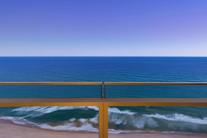 Une vue sur la plage, avec un ciel dégagé, des vagues sur l’océan et une rambarde jaune.