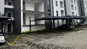 A multi-story residential building with balconies, a parking area with marked spaces, and a covered carport. - Stylish 1BR Midrand Pool, Wifi & Secure Parking (Johannesburg)