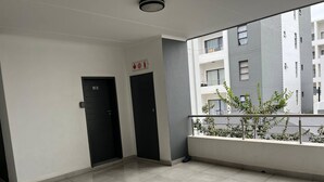 A clean, modern hallway with two black doors, one marked with the number 193, and a balcony with a metal railing overlooking a building. - Stylish 1BR Midrand Pool, Wifi & Secure Parking (Johannesburg)