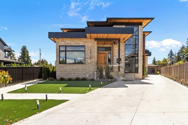 A modern two-story house with a brick facade, large windows, and a wooden deck. - Premium Villa for Family Reunions & Wedding Stays (Surrey)