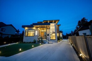 A modern two-story house with a well-lit entrance, a visible garage, and a paved driveway. - Premium Villa for Family Reunions & Wedding Stays (Surrey)