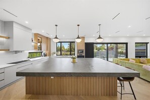 Une cuisine moderne dotée d’un grand îlot central, de luminaires suspendus et offrant une vue sur l’extérieur.