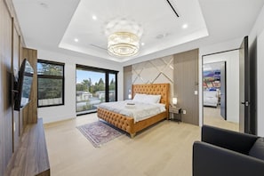 Une chambre à coucher moderne avec un grand lit, un lustre, une télévision et une vue sur l’extérieur.