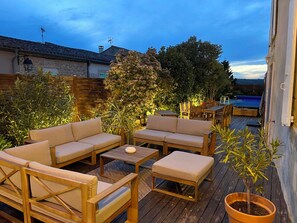 Een houten terras met buitenmeubilair, een zwembad en een stenen muur.