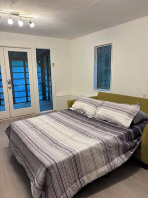 A bedroom with a bed, a window, and a door leading to an outdoor area.