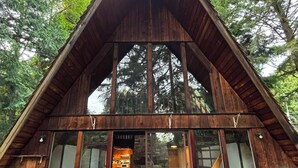 Eine Holzhütte mit einem dreieckigen Dach, großen Glasfenstern und einer Holzterrasse.