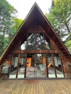 A wooden cabin with a triangular roof, large glass windows, and a wooden deck. - Cozy Chalet close to Mountains & Ocean (West Vancouver)