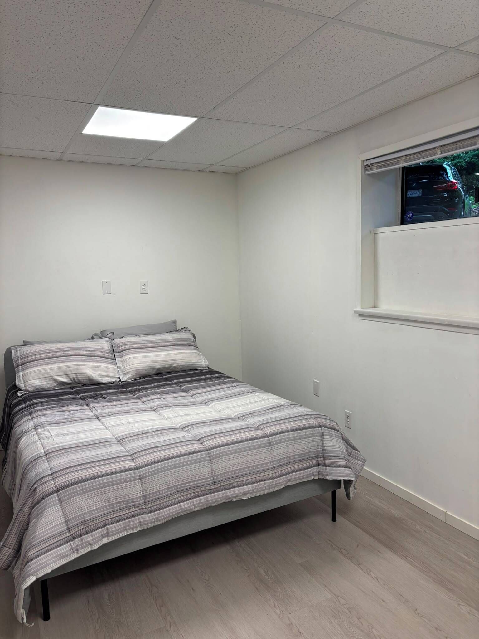 Une chambre à coucher avec un lit, une fenêtre et un luminaire au plafond.