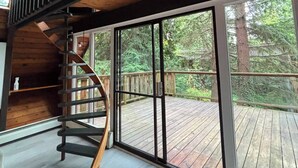 Ein geräumiges Zimmer mit großem Fenster, einer Holzterrasse davor und einer Wendeltreppe.