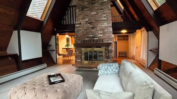 A loft-style room with a stone fireplace, a tufted ottoman, and a white sofa.