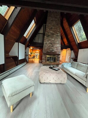 Un loft espacioso con techos altos, vigas de madera a la vista, chimenea de piedra y vista a la cocina a través de una puerta abierta.