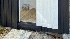 A wooden shed with a white door, a small window, and a shelf with a basket inside. - House by a secluded lake in rural Blekinge (Hallabro)