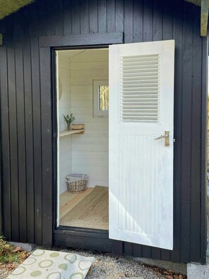 A wooden shed with a white door, a small window, and a shelf with a basket inside. - House by a secluded lake in rural Blekinge (Hallabro)