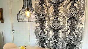 A dining area with a light wooden table, wicker chairs, a patterned wall, and a hanging light fixture. - House by a secluded lake in rural Blekinge (Hallabro)