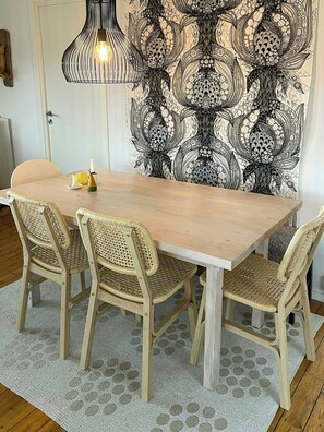 A dining area with a light wooden table, wicker chairs, a patterned wall, and a hanging light fixture. - House by a secluded lake in rural Blekinge (Hallabro)