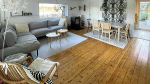 A cozy living room with a sofa, two round tables, a dining table with chairs, a fireplace, and a large abstract wall art piece. - House by a secluded lake in rural Blekinge (Hallabro)